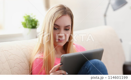 young beautiful blond woman sit on the sofa in livingroom hold tablet in arms 114601199