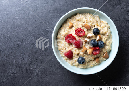 Oatmeal porridge with raspberries, blueberries and almonds in bowl on black background. Top view Oatmeal porridge with raspberries, blueberries and almonds in bowl on black background. Top view 114601299