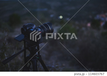 A black digital semi-mirror camera photographic equipment, with movable mockup touch screen, placed on tripod in nature, capturing steady picture or recording video of the city in the night and dawn. A black digital semi-mirror camera photographic equipment, with movable mockup touch screen, placed on tripod in nature, capturing steady picture or recording video of the city in the night and dawn. 114603767