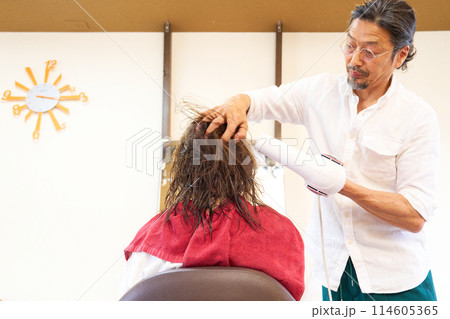 ドライヤーで髪を乾かす男性スタイリストと女性客 ドライヤーで髪を乾かす男性スタイリストと女性客 114605365