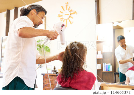 ドライヤーで髪を乾かす男性スタイリストと女性客 114605372