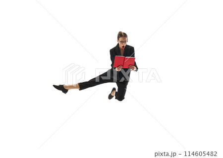 Emotional businesswoman in motion, in mid-air pose jumping with shocked face and looking in book, notes isolated on white background 114605482