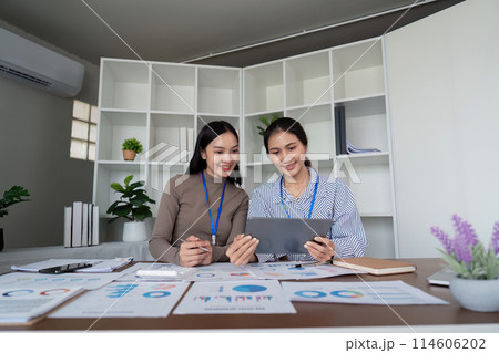 Two Asian women collaborating on a project in a modern office. Concept of teamwork, business, and productivity Two Asian women collaborating on a project in a modern office. Concept of teamwork, business, and productivity 114606202