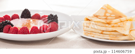 Breakfast of raspberries and blackberries with yogurt and pancakes on table 114606759