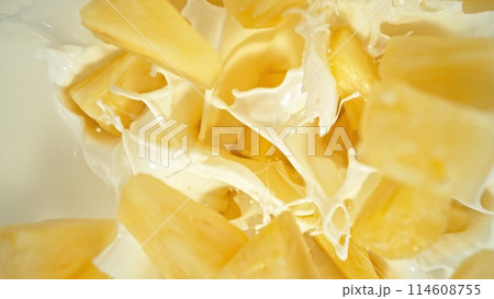 Fresh pineapple pieces falling into cream, top down view 114608755