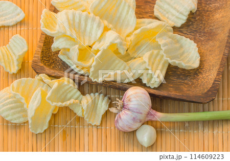 Crispy potato chips in a wooden bowl next to garlic bulb Crispy potato chips in a wooden bowl next to garlic bulb 114609223