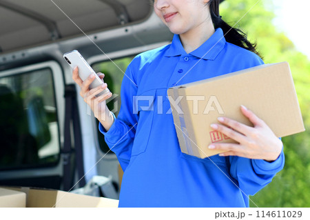 荷物を持ちスマホを見る配送ドライバー女性 114611029
