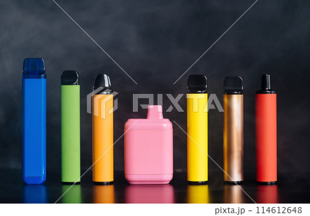 A set of colorful disposable electronic cigarettes of different shapes on a black background with smoke. Concept of modern smoking, vaping and nicotine. A set of colorful disposable electronic cigarettes of different shapes on a black background with smoke. Concept of modern smoking, vaping and nicotine. 114612648
