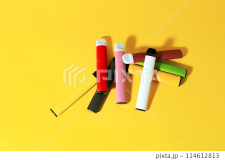 Layout of colorful disposable electronic cigarettes with shadows on a yellow background. The concept of modern smoking, vaping and nicotine. Top view Layout of colorful disposable electronic cigarettes with shadows on a yellow background. The concept of modern smoking, vaping and nicotine. Top view 114612813