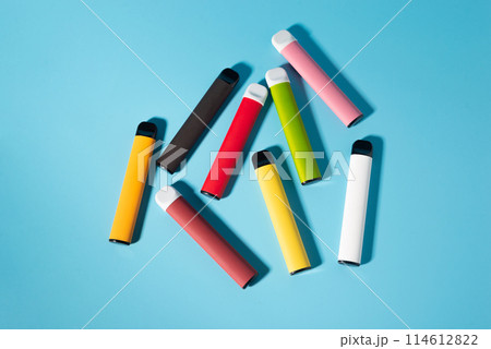 Layout of colorful disposable electronic cigarettes with shadows on a blue background. The concept of modern smoking, vaping and nicotine. Top view Layout of colorful disposable electronic cigarettes with shadows on a blue background. The concept of modern smoking, vaping and nicotine. Top view 114612822