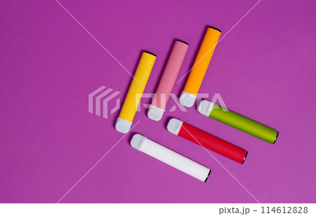 Colorful disposable electronic cigarettes on a purple background. The concept of modern smoking, vaping and nicotine. Top view. 114612828