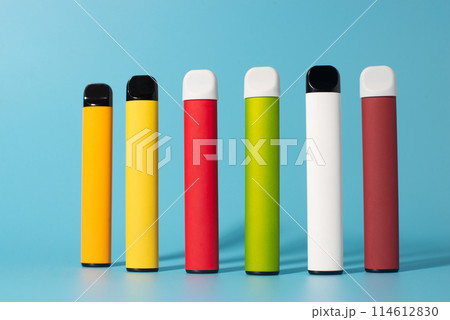 Set of colorful disposable electronic cigarettes with shadows on a blue background. The concept of modern smoking, vaping and nicotine. Top view Set of colorful disposable electronic cigarettes with shadows on a blue background. The concept of modern smoking, vaping and nicotine. Top view 114612830