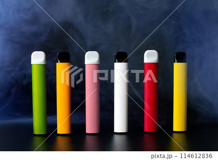 Set of colorful disposable electronic cigarettes on a black background with smoke. The concept of modern smoking, vaping and nicotine. Set of colorful disposable electronic cigarettes on a black background with smoke. The concept of modern smoking, vaping and nicotine. 114612836