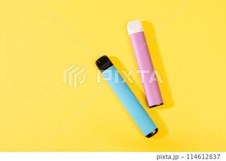 disposable electronic cigarettes with shadow on a yellow background with copy space. The concept of modern smoking, vaping and nicotine. top view. disposable electronic cigarettes with shadow on a yellow background with copy space. The concept of modern smoking, vaping and nicotine. top view. 114612837