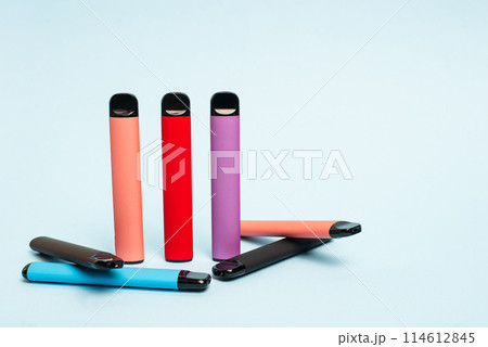Layout of colorful disposable electronic cigarettes on a light blue background. The concept of modern smoking, vaping and nicotine. Layout of colorful disposable electronic cigarettes on a light blue background. The concept of modern smoking, vaping and nicotine. 114612845