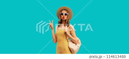 Beautiful blonde young woman blowing a kiss posing wearing summer hat, backpack on blue background 114613480