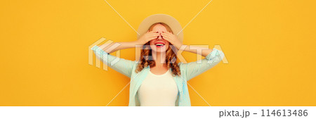 Stylish surprised young woman covering her eyes with hands in summer straw hat on yellow background 114613486