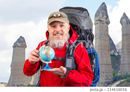 bearded tourist in a red jacket holds a model of the world globe in his hands 114618038