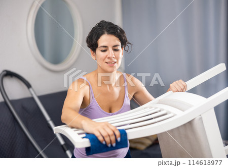 Latino woman doing cleaning in the room - dusting chair 114618977