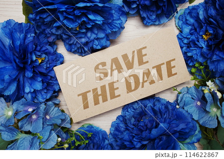 Save the Date text message on paper card with flowers border frame on wooden background 114622867