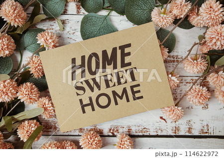 Home Sweet Home text message on paper card with flowers border frame on wooden background 114622972