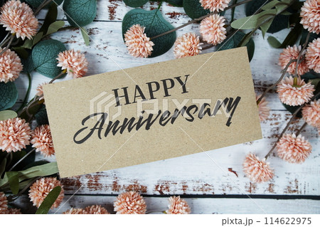 Happy Anniversary text message on paper card with flowers border frame on wooden background Happy Anniversary text message on paper card with flowers border frame on wooden background 114622975