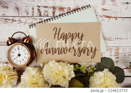 Happy Anniversary text message on paper card with flowers border frame on wooden background 114623755