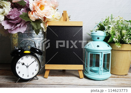 Easel mockup with blue landtern, alarm clock and flowers bouquet decoration on wooden background Easel mockup with blue landtern, alarm clock and flowers bouquet decoration on wooden background 114623773