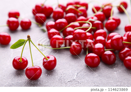 Fresh sweet cherries with leaves on grey concrete background, top view Fresh sweet cherries with leaves on grey concrete background, top view 114623869