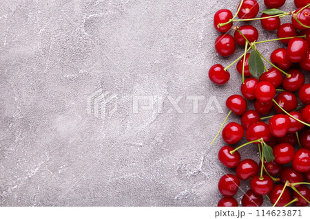 Fresh sweet cherries with leaves on grey concrete background, top view Fresh sweet cherries with leaves on grey concrete background, top view 114623871