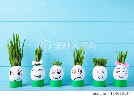 Cute handmade eggs with hair of green grass with copy space. Easter concept on blue background Cute handmade eggs with hair of green grass with copy space. Easter concept on blue background 114626124