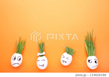 Cute handmade eggs with hair of green grass with copy space. Easter concept on orange background 114626166