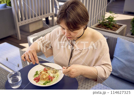 medium sized woman in peach fuzz dress eating cottage cheese pancakes with salmon and spinach in modern restaurant medium sized woman in peach fuzz dress eating cottage cheese pancakes with salmon and spinach in modern restaurant 114627325