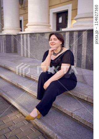 a medium-sized woman in a black corset near a theater with antique columns 114627360