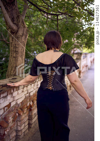 a    medium size woman in a black corset and wide leg trousers walks through the city in the morning light 114627361