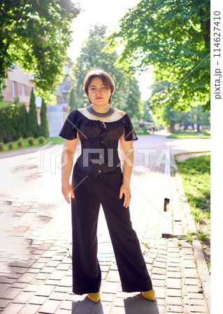 a    medium size woman in a black corset and wide leg trousers walks through the city in the morning light 114627410