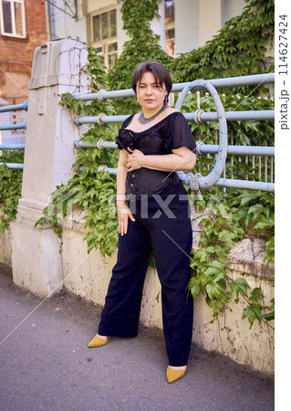 a medium size woman in a black corset and wide leg trousers walks through the city in the morning light a medium size woman in a black corset and wide leg trousers walks through the city in the morning light 114627424
