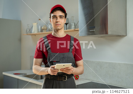 Professional Repairman in Red Uniform Using Tablet in Modern Kitchen During Daytime Professional Repairman in Red Uniform Using Tablet in Modern Kitchen During Daytime 114627521