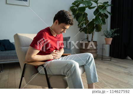 Young Man Experiencing Stomach Pain in a Modern Living Room Setting Young Man Experiencing Stomach Pain in a Modern Living Room Setting 114627592