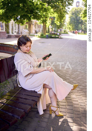 a plus size woman in peach fuzz dress talking on phone in morning city 114627764