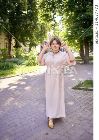 plus size woman in peach fuzz dress with hat having fun on morning city streets 114627773