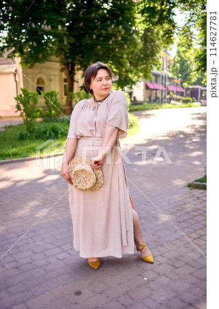 plus size woman in peach fuzz dress with hat having fun on morning city streets 114627781