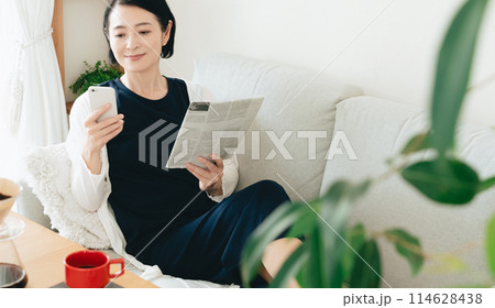 スマホと英字新聞を見るミドル女性 114628438