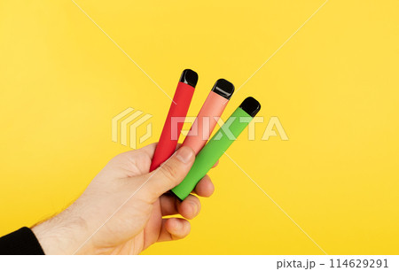 Disposable electronic cigarettes of different flavors in hand on a yellow background. The concept of modern smoking, vaping and nicotine 114629291