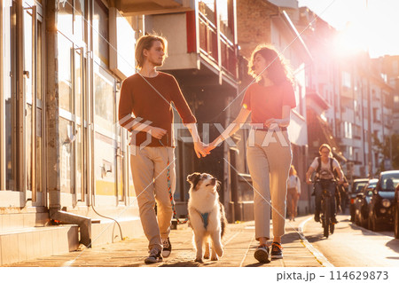 Happy married couple is walking around city with their Aussie dog. Sunset light in background 114629873