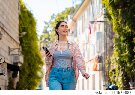 Portrait of happy pretty young Caucasian woman walks through an old Mediterranean city with an online guide on her smartphone. Summer vacation Portrait of happy pretty young Caucasian woman walks through an old Mediterranean city with an online guide on her smartphone. Summer vacation 114629882