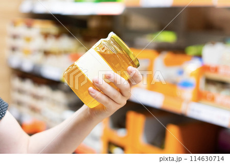 Young male hand holds honey on a blurred background, a row of shelves with groceries in supermarket 114630714