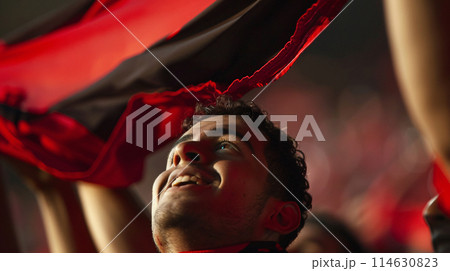 a soccer fan, their eyes shining with passion as they raise their scarf high in the air 114630823