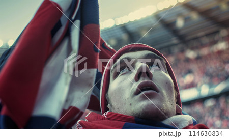 a soccer fan, their eyes shining with passion as they raise their scarf high in the air 114630834