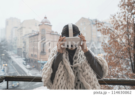 A charming woman in VR glasses marvels at the winter city scene around her. 114630862